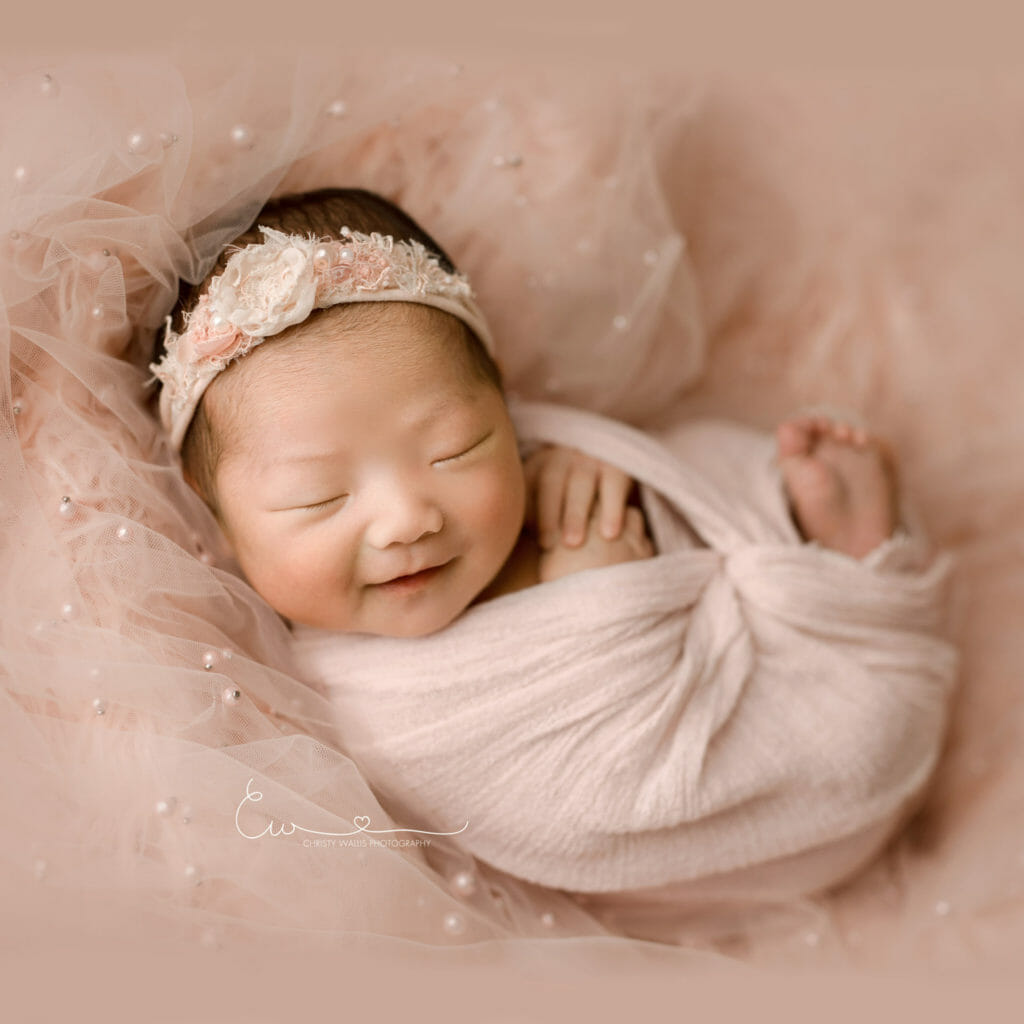 San Diego newborn baby girl with pink headband and pearls Best San Diego Newborn Photographer Beautiful newborn baby wrapped in cozy natural props in San Diego Rancho Bernardo studio Photographer cute Newborn baby swaddled in soft blanket